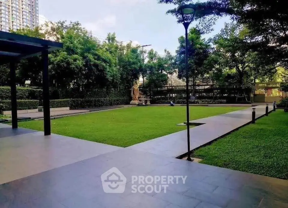 Spacious garden area in modern residential complex with lush greenery and paved walkways.