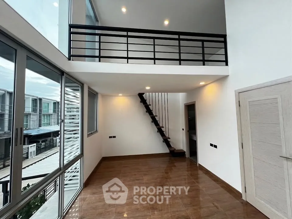 Spacious modern loft with high ceilings and mezzanine, featuring large windows and sleek staircase.