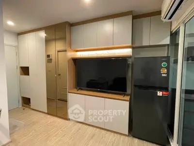 Modern living room with sleek cabinetry and large TV, featuring a stylish refrigerator and air conditioning unit.