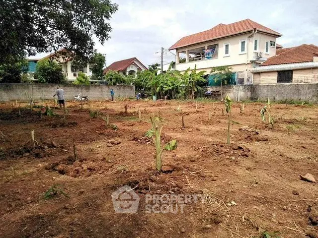 Spacious residential plot with potential for development, surrounded by lush greenery and nearby homes.