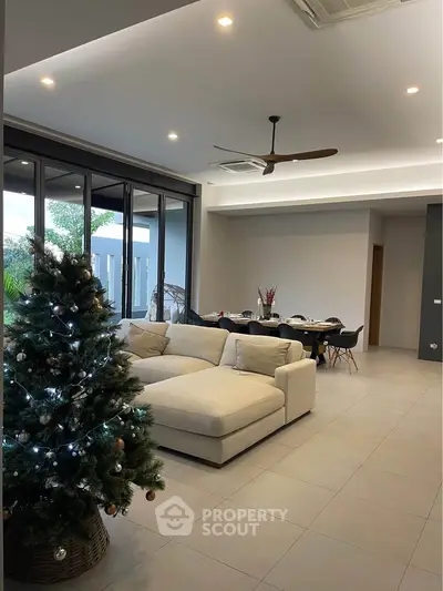 Spacious modern living room with large windows and elegant decor, featuring a cozy sofa and festive Christmas tree.