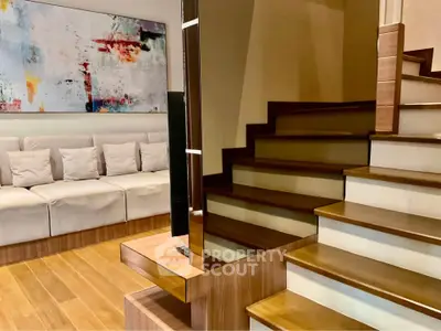 Modern living room with stylish staircase and abstract art, featuring cozy seating and wooden flooring.