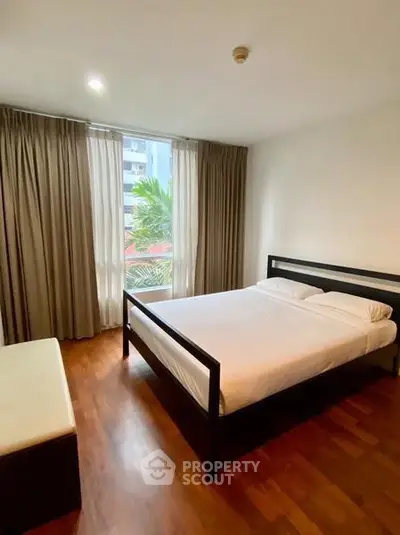 Spacious bedroom with large window and elegant wooden flooring in modern apartment.