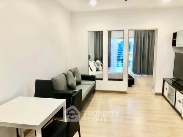 Modern living room with sleek furniture and wooden flooring, leading to a cozy bedroom.