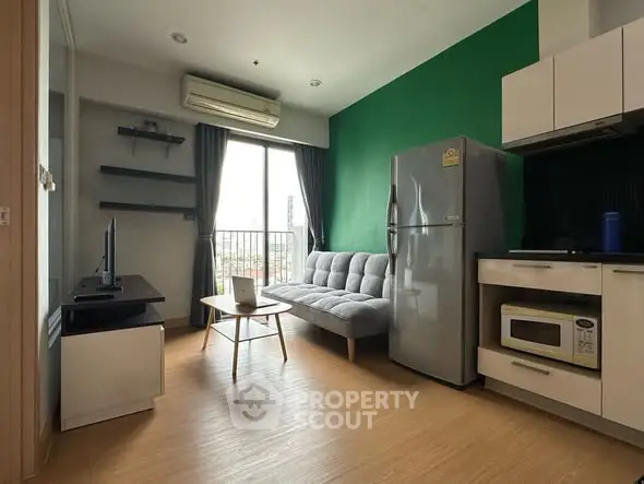Modern living room with green accent wall, cozy sofa, and sleek kitchen appliances in a bright apartment.