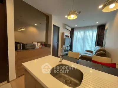 Modern living room with open kitchen, featuring stylish lighting and cozy seating area.