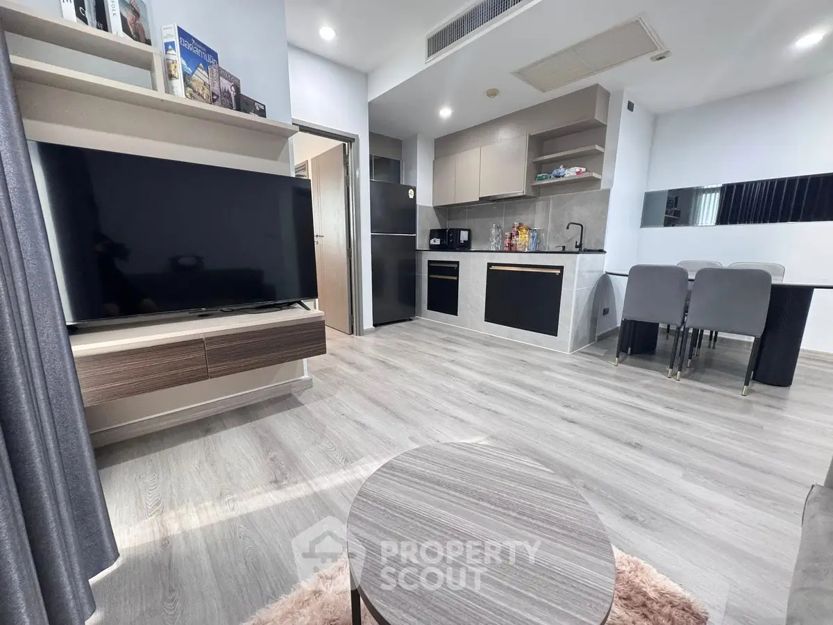 Modern open-layout living room with sleek kitchen and dining area, featuring contemporary furniture and appliances.