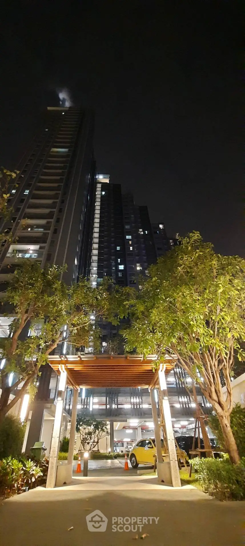 Stunning night view of modern high-rise building with illuminated entrance and lush greenery.