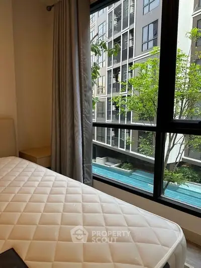 Cozy bedroom with large window overlooking modern apartment complex and pool.