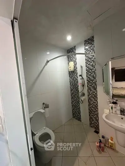 Modern bathroom with tiled walls and shower area, featuring essential amenities.