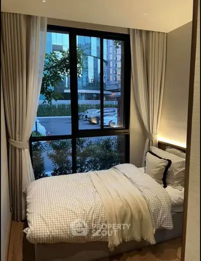 Cozy bedroom with large window offering city view, perfect for urban living.