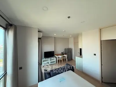 Modern living room with open kitchen and dining area, featuring sleek furniture and large windows.