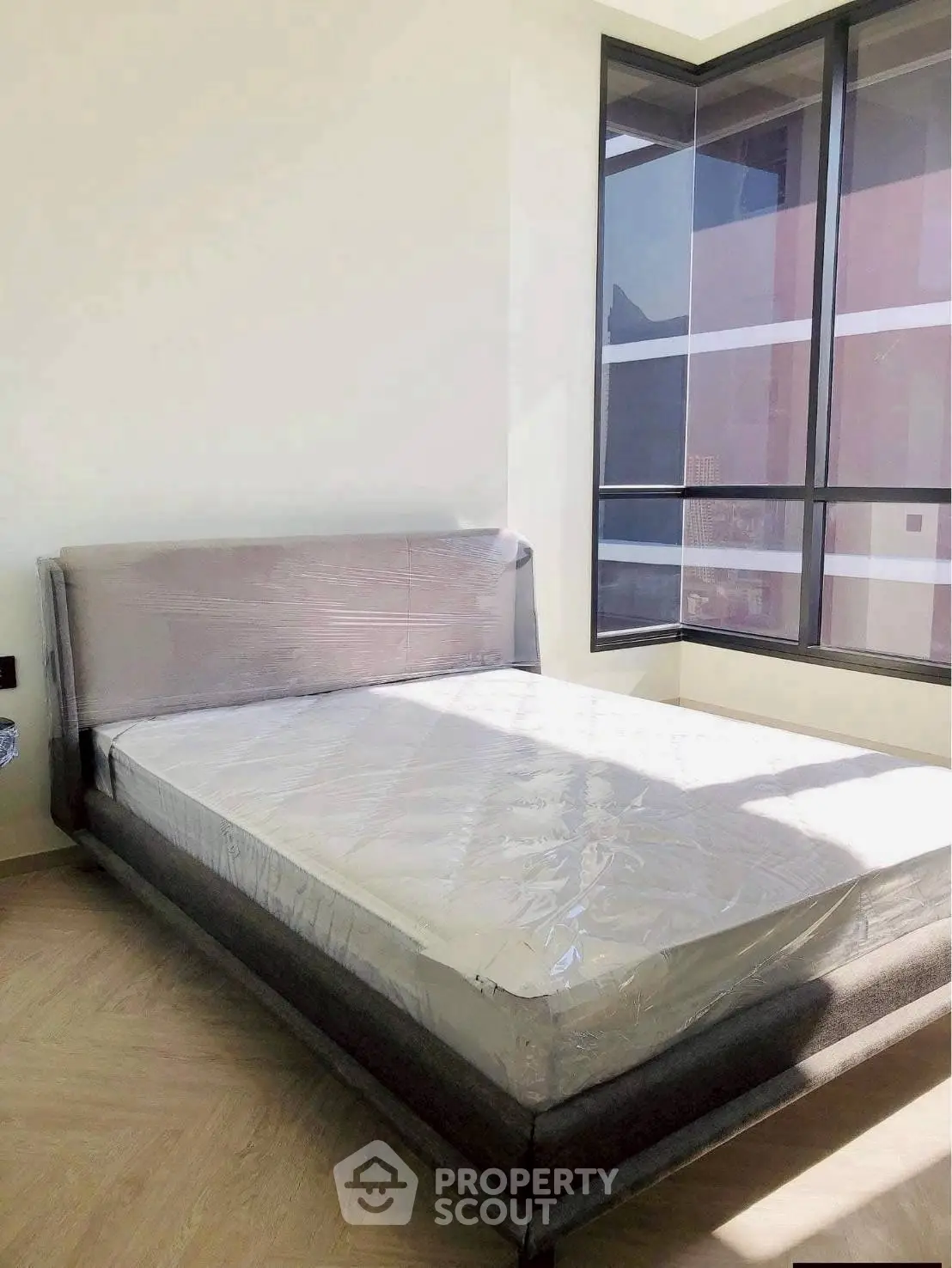 Modern bedroom with large windows and natural light, featuring a new bed and stylish flooring.