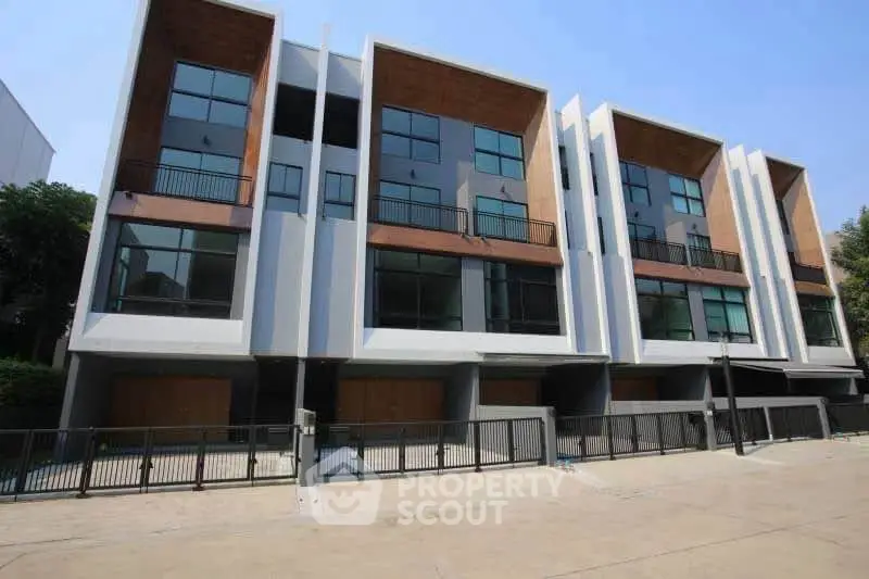 Modern multi-story townhouses with large windows and balconies in a sunny neighborhood.