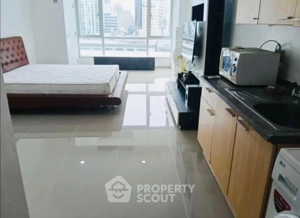 Modern studio apartment with open layout, featuring a cozy bed, kitchenette, and city view.