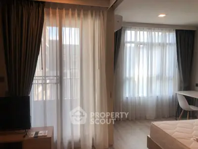 Bright modern bedroom with large windows and elegant curtains, featuring a cozy seating area and stylish decor.