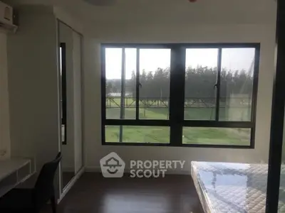 Bright bedroom with large windows offering scenic views of greenery, featuring a comfortable bed and study desk.