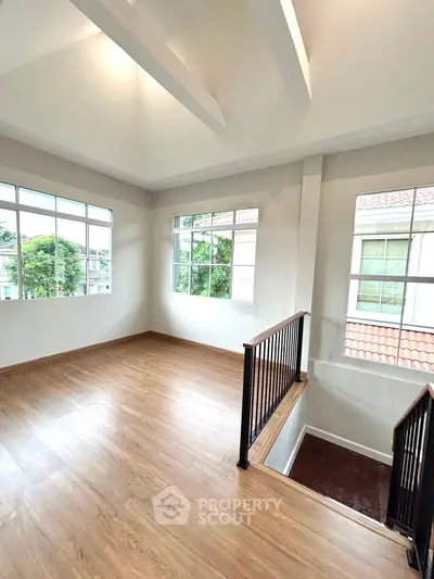 Spacious and bright room with large windows and wooden flooring, perfect for a home office or study area.