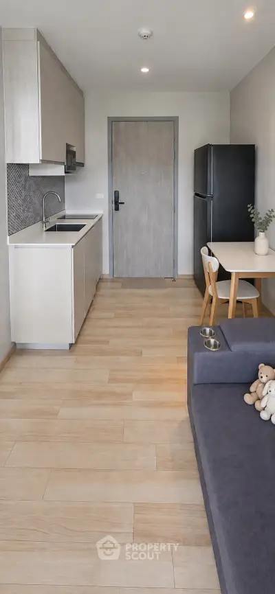Modern studio apartment with open kitchen and cozy living area, featuring sleek cabinetry and light wood flooring.