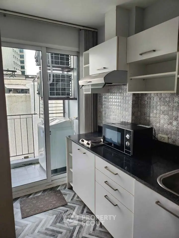 Modern kitchen with sleek cabinets, microwave, and balcony access in urban apartment.