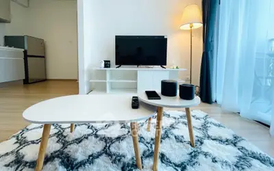 Modern living room with stylish furniture and natural light, featuring a cozy rug and sleek TV setup.