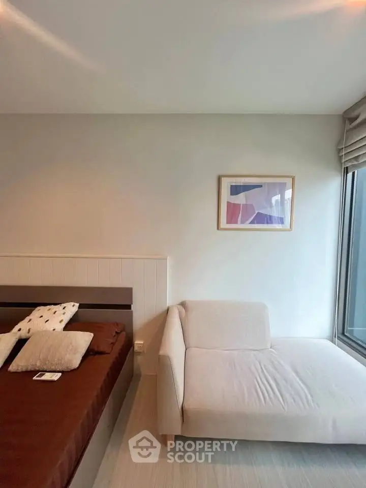 Modern bedroom with cozy bed and stylish chaise lounge by large window.