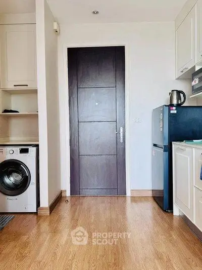 Modern kitchen with wooden flooring, washing machine, and compact fridge.