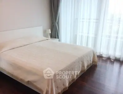 Spacious bedroom with large windows and elegant curtains, featuring a comfortable bed and wooden flooring.