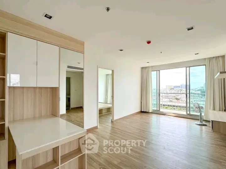 Spacious modern living room with large windows and wooden flooring, offering a stunning city view.