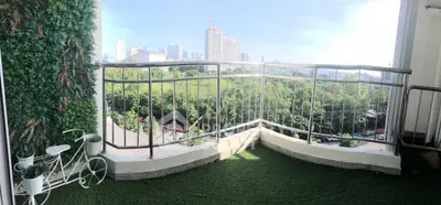 Spacious balcony with lush greenery and city skyline view, perfect for relaxation and enjoying urban living.