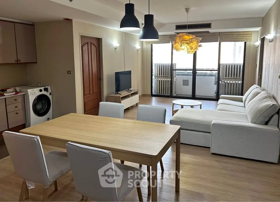 Spacious living room with modern furniture and natural light, featuring a washing machine and open layout.
