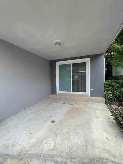 Spacious covered patio with sliding glass doors and garden view, perfect for outdoor relaxation.