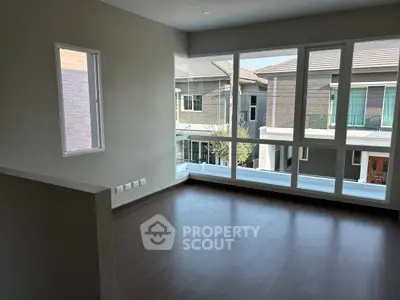 Spacious empty room with large windows offering a view of modern houses, perfect for customization.