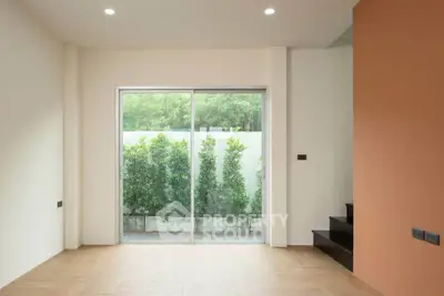 Modern living room with large sliding glass doors opening to a lush garden view, featuring sleek wooden flooring.