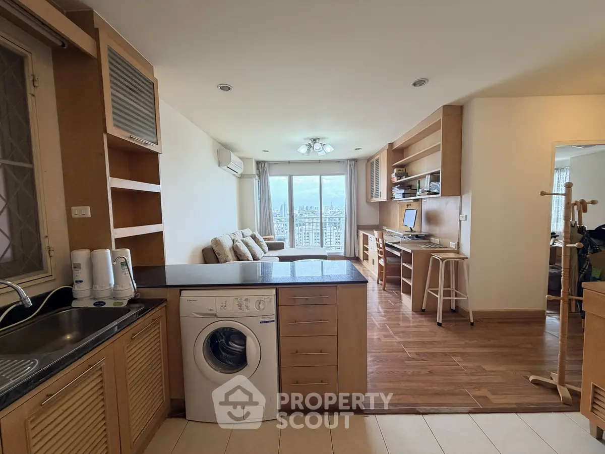 Modern open-plan living room with kitchen and city view, featuring wooden flooring and built-in shelves.