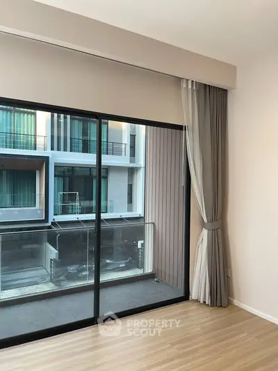 Modern apartment with large sliding glass doors opening to a balcony, offering a view of contemporary architecture.