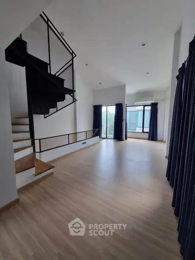 Spacious modern living room with sleek staircase and large windows for natural light.