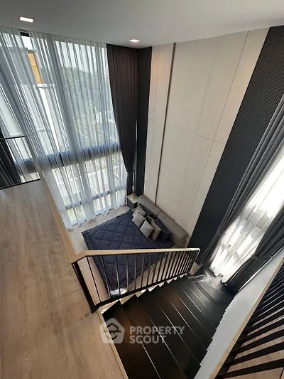 Modern loft-style living room with high ceilings and large windows, featuring a cozy seating area and elegant decor.