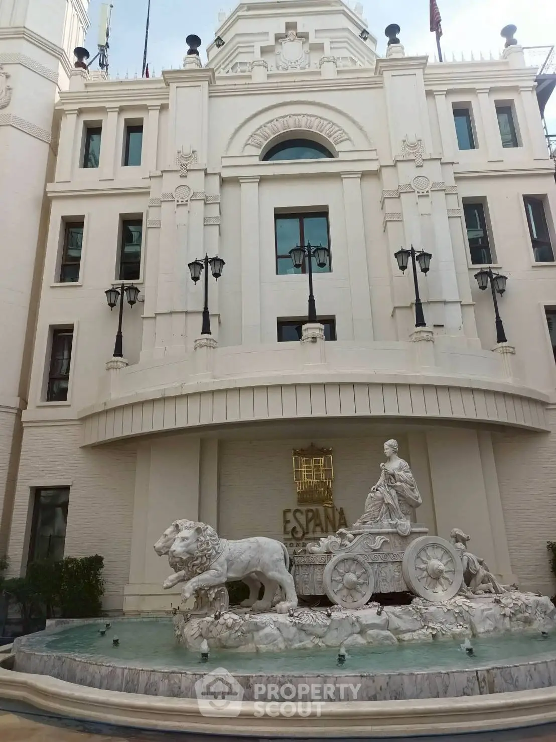 Elegant building facade with a grand fountain featuring a lion and chariot sculpture.