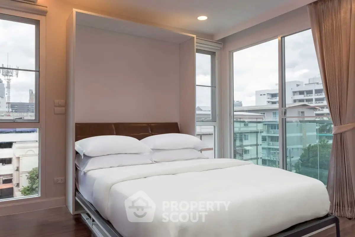 Modern bedroom with large windows and city view, featuring a cozy bed and elegant curtains.
