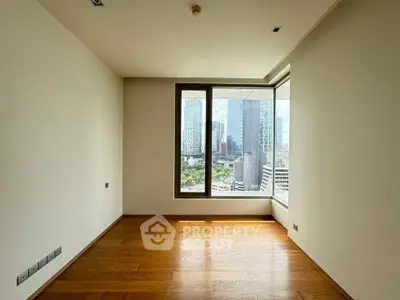 Spacious room with wooden flooring and cityscape view through large window.