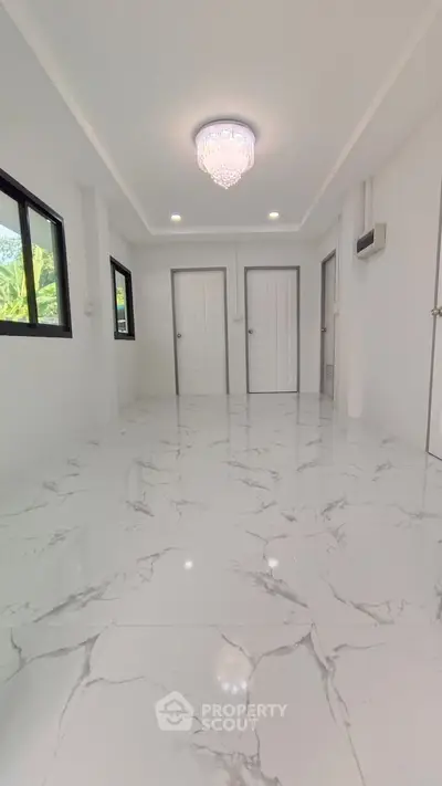 Spacious modern room with elegant marble flooring and chandelier lighting.