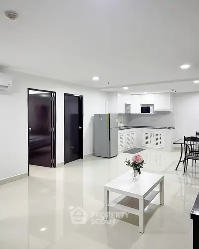 Modern open-layout living room with sleek kitchen and dining area, featuring contemporary furniture and bright lighting.