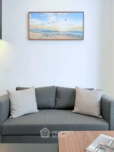 Modern living room with stylish gray sofa and beach artwork on wall.