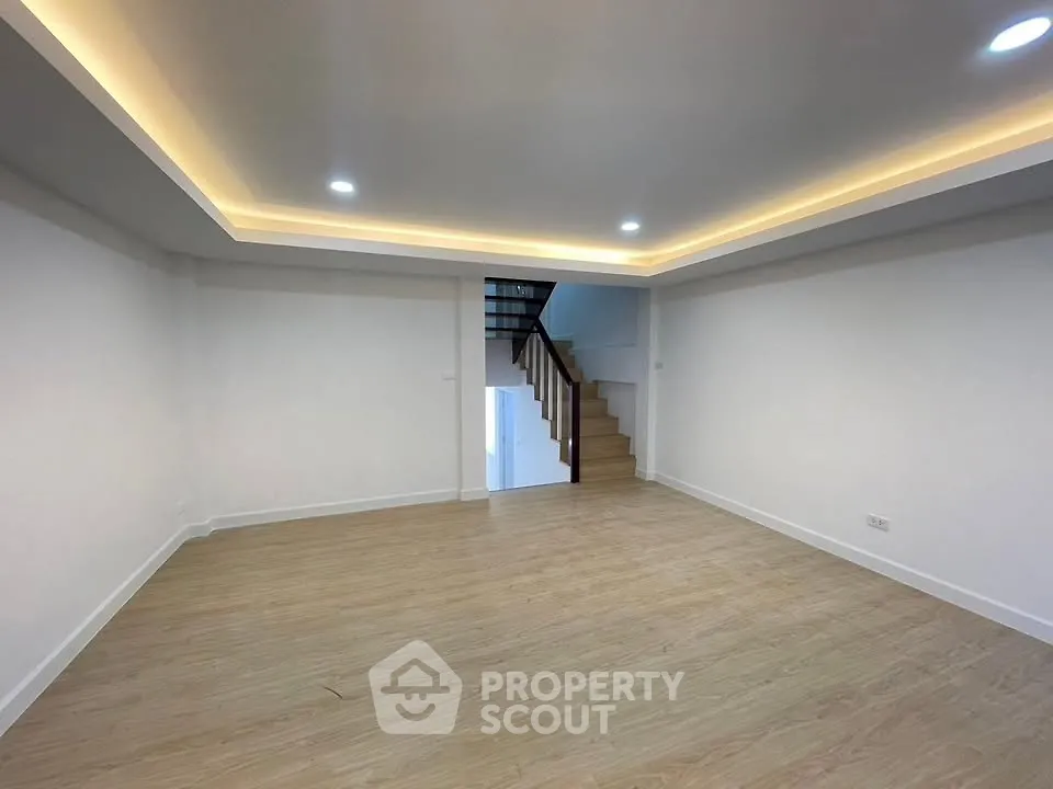 Spacious modern living room with recessed lighting and wooden flooring, featuring a staircase leading to the upper level.