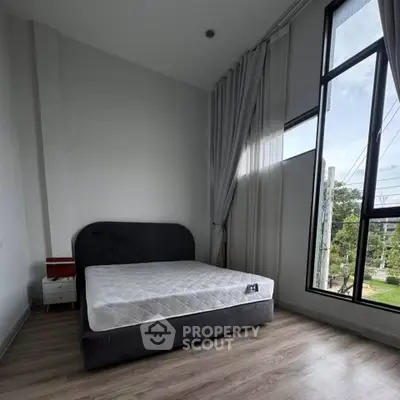 Spacious bedroom with large window and modern furnishings, offering ample natural light and a serene atmosphere.