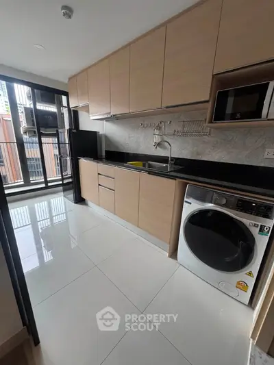 Modern kitchen with sleek cabinetry, washing machine, and balcony access in a stylish apartment.