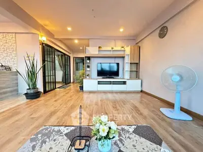 Spacious living room with modern decor and wooden flooring, featuring a TV unit and stylish furnishings.