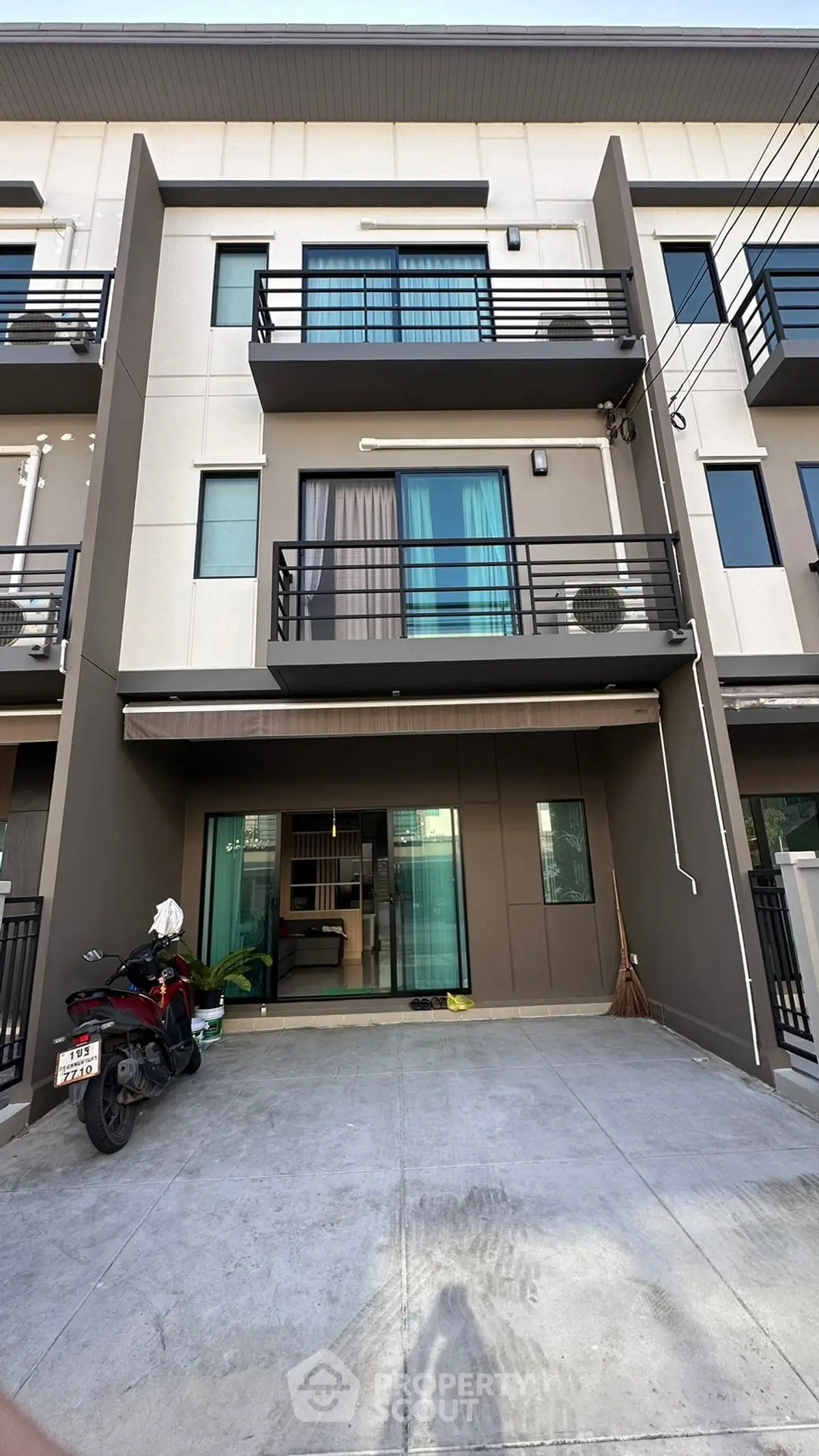 Modern three-story townhouse with balcony and parking space in urban setting.