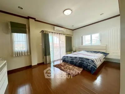Spacious bedroom with wooden flooring and large windows offering natural light.
